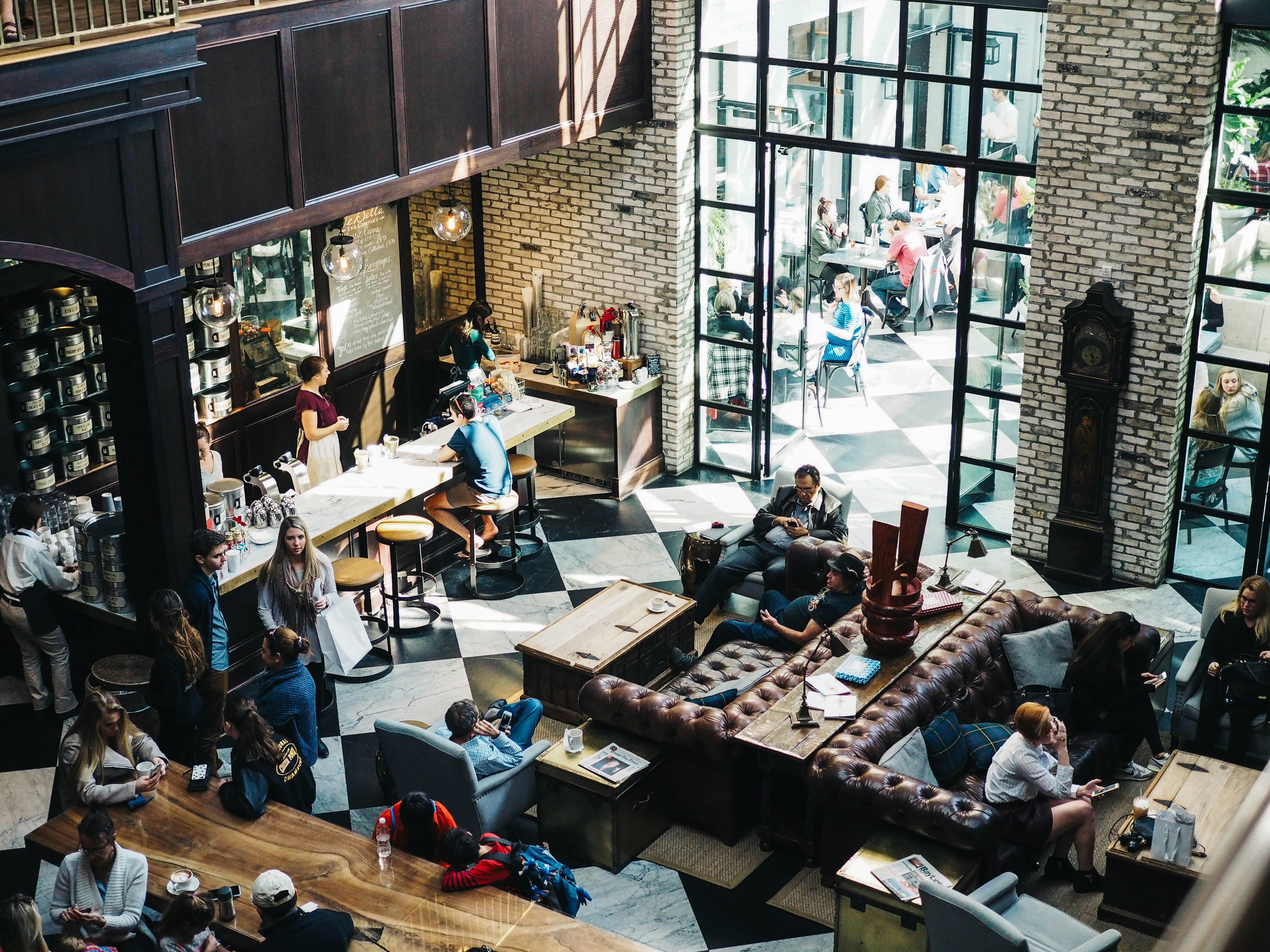 Belebtes Café im Industrial Style mit Ledersofas, Backsteinwänden und großen Sprossenfenstern